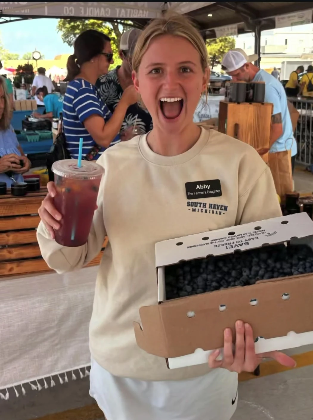 A person holding a berry-colored drink and fresh blueberries at an outdoor event