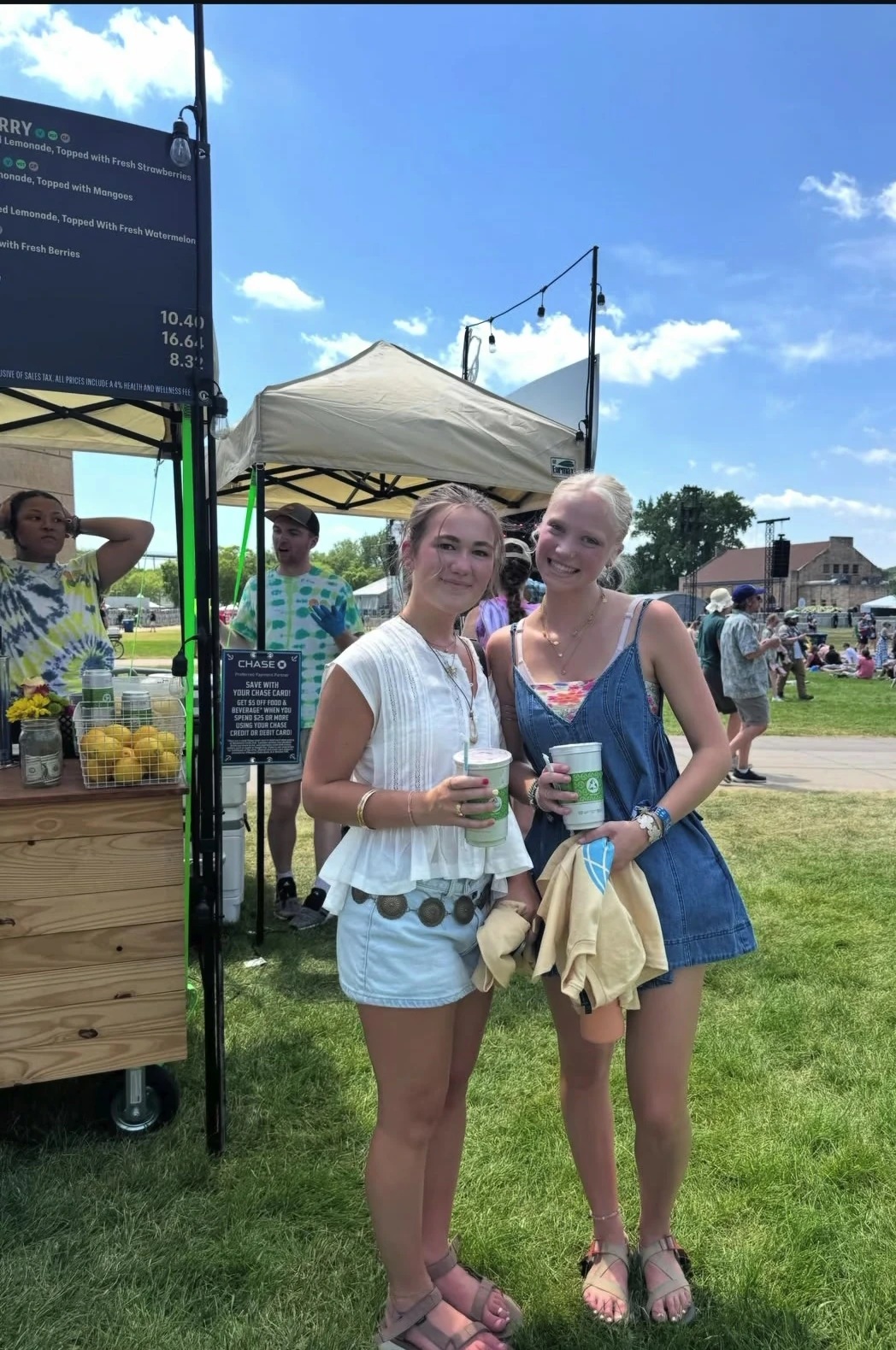 Two festival guests holding branded lemonade cups on a sunny grassy event lawn