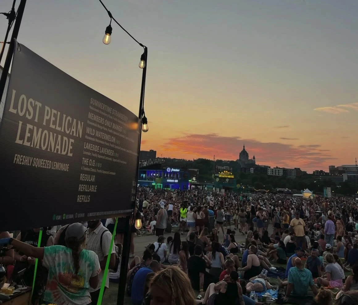 Lost Pelican Lemonade signage and string lights overlooking an outdoor festival crowd at sunset